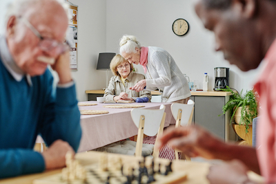 Senior women discussing the way of knitting while senior men playing chess in nursing home
