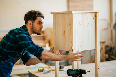 profession, carpentry, woodwork and people concept - young carpenter testing wood plank evenness at workshop