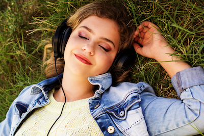 Young happy teenager is wearing headphones lying on the grass