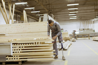 Disabled young man with an artificial leg is working at the furniture factory