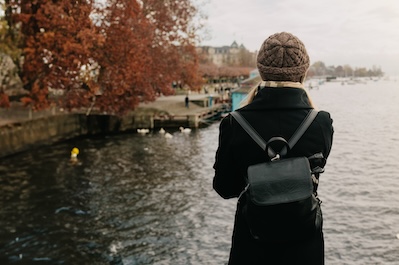Young beautiful pretty blonde tourist girl in warm hat and coat with backpack walking at cold autumn in Europe city enjoying her travel in Zurich Switzerland
