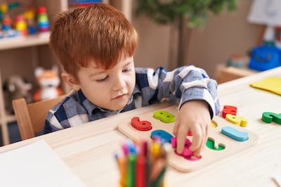 Adorable toddler playing with maths puzzle game sitting on table at classroom