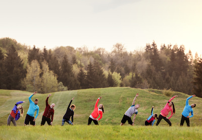 A large group of active multi generation people running a race competition in nature, stretching.