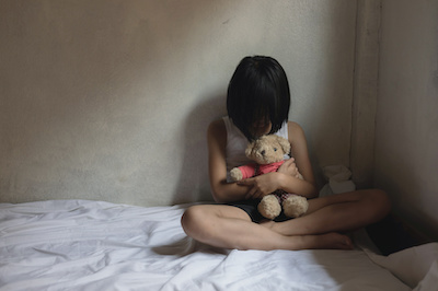 Lonely scared little girl sitting in bed room, hugging her teddy bear and crying. Child abuse
