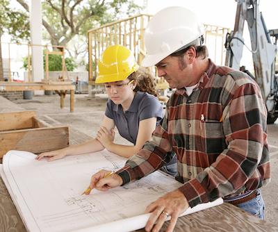 An engineer and a female student going over blueprints on a construction site.  