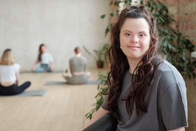 Brunette female looking at you while group of girls practicing yoga in gym