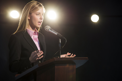 Young businesswoman giving speech at podium in auditorium